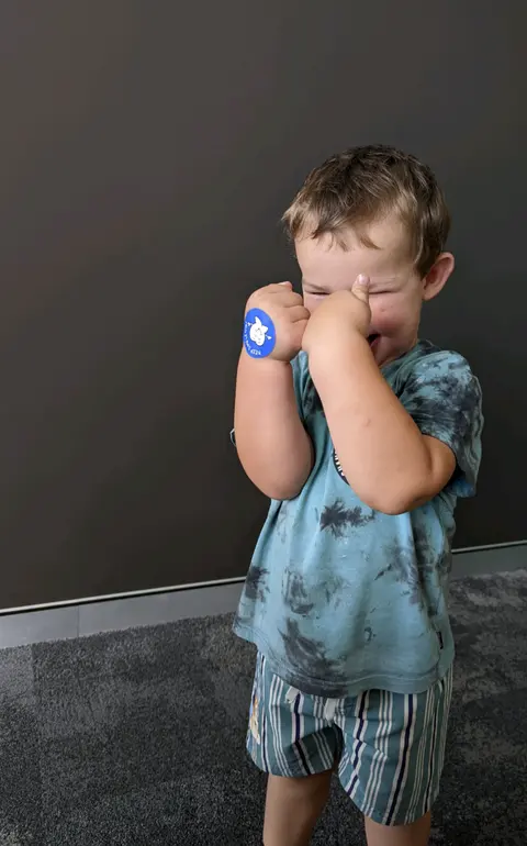A young boy giggling behind his hands, proudly wearing his sticker after a visit to Southside Dental Toowoomba